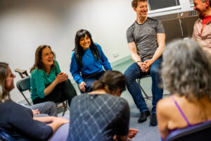 group of people sat around on chairs in a cirlce, variying stages of smiles and laughter