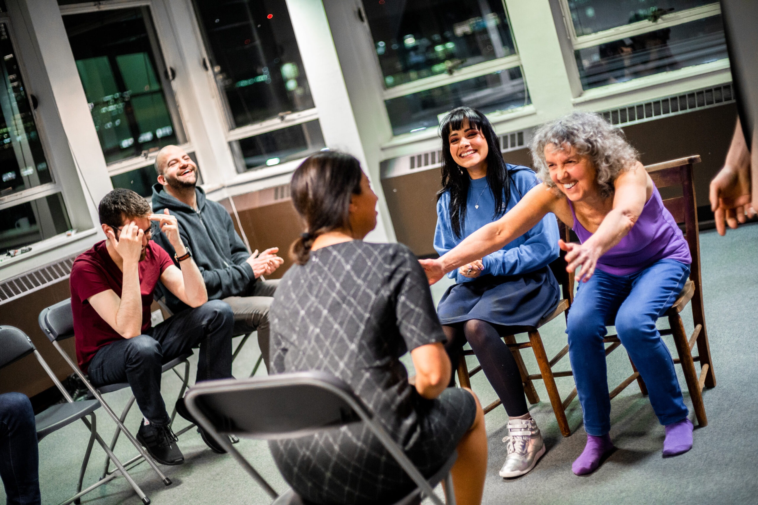 5 improvisers sit in a circle laughing during an AndAlso improv workshop